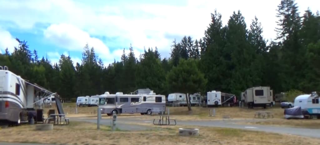 RVs parked in rows surrounded by trees under a cloudy sky at North Whidbey RV Park