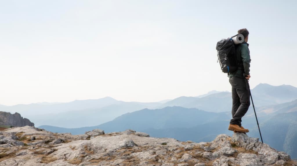 A lone hiker stands on a mountain crest, overlooking a range