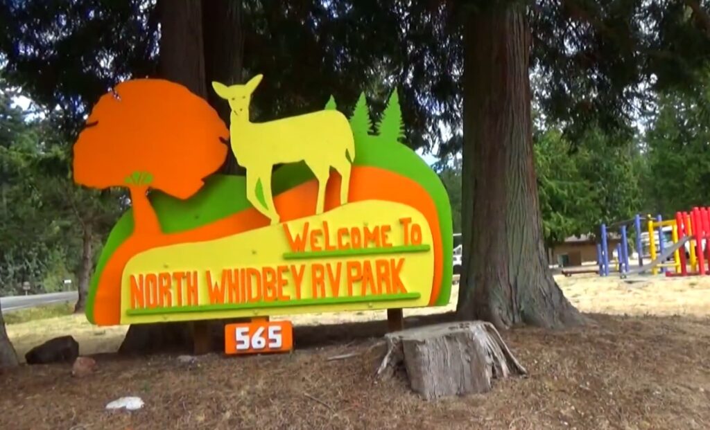welcome sign featuring a deer silhouette at North Whidbey RV Park with playground in the background