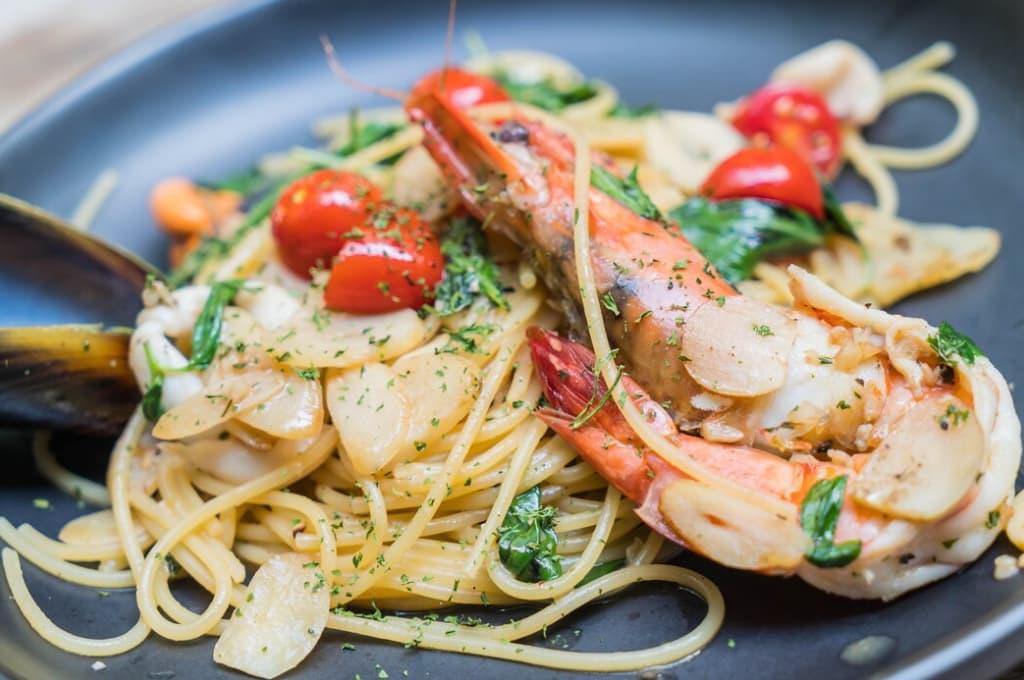 Spaghetti with seafood, herbs, and tomatoes on a dark plate