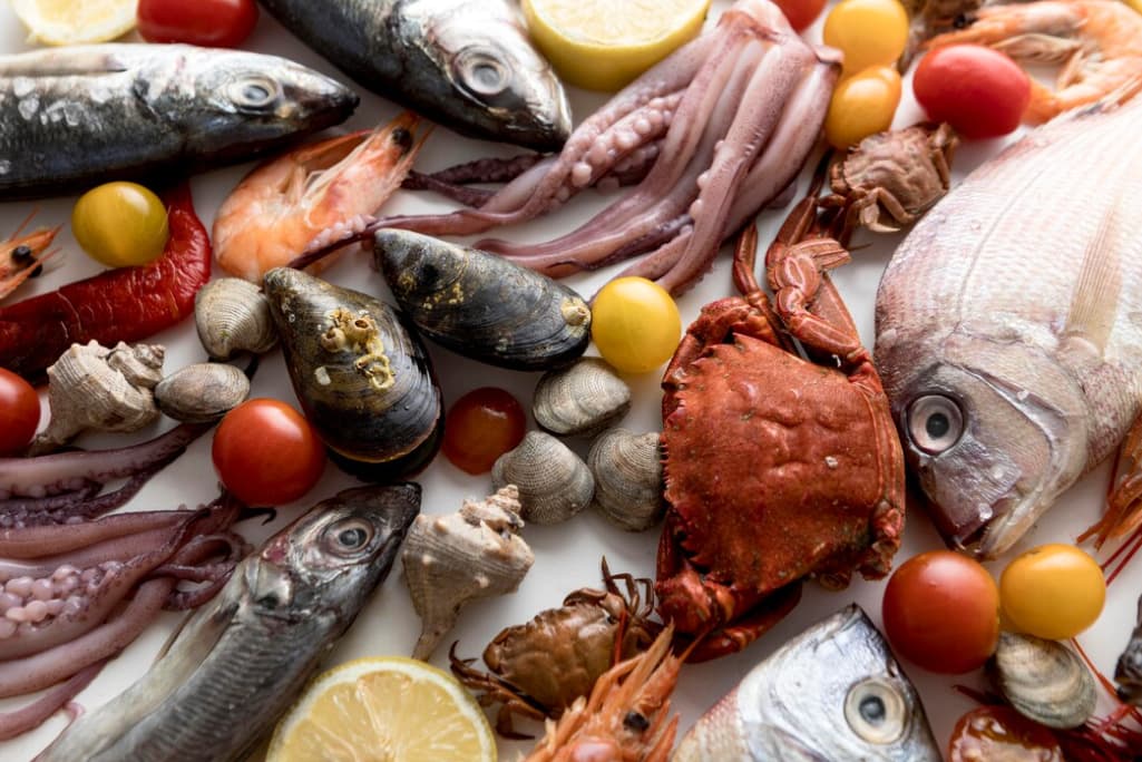 Assorted raw seafood with lemons and tomatoes on a white surface